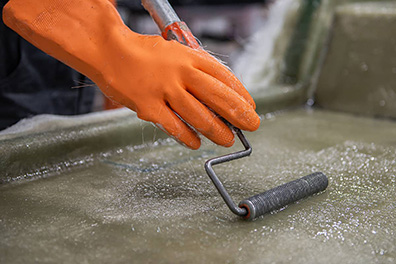 Hand of a factory worker in a glove using laminating roller to press the fabric into the resin, removing air bubbles and ensuring even distribution